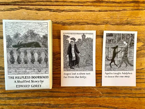 The Helpless Doorknob by Edward Gorey box set and illustrated story cards on wood table