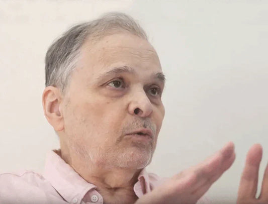 Older man in a light pink shirt gesturing, neutral background, Edward Gorey Online Shop context