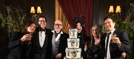 Group celebrating around ornate tiered cake, Edward Gorey themed party, formal attire