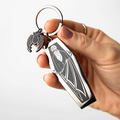 Hand holding Edward Gorey Dracula coffin keychain with bat charm, gothic art accessory