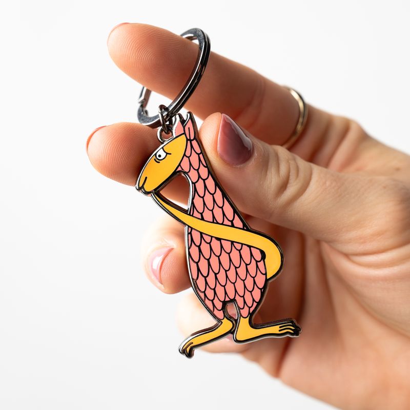 Hand holding Edward Gorey Fantod creature keychain with pink scales and yellow accents