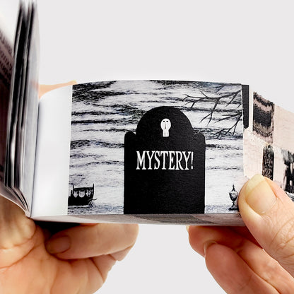 Edward Gorey flipbook with black tombstone illustration and 'MYSTERY!' text, held in hand