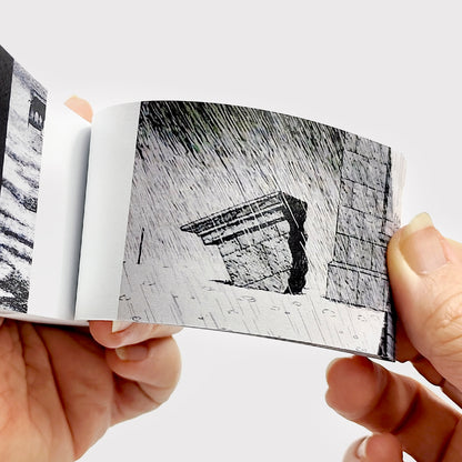Hand flipping through Edward Gorey mystery flipbook with black and white illustrated scene