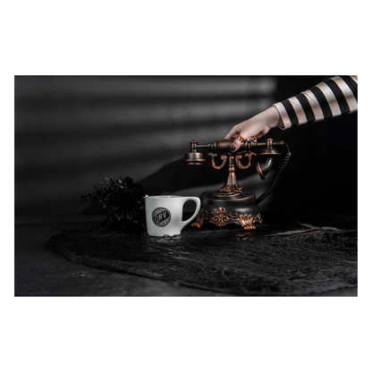 Edward Gorey style Q-R-V Catastrophe mug beside vintage telephone on dark table