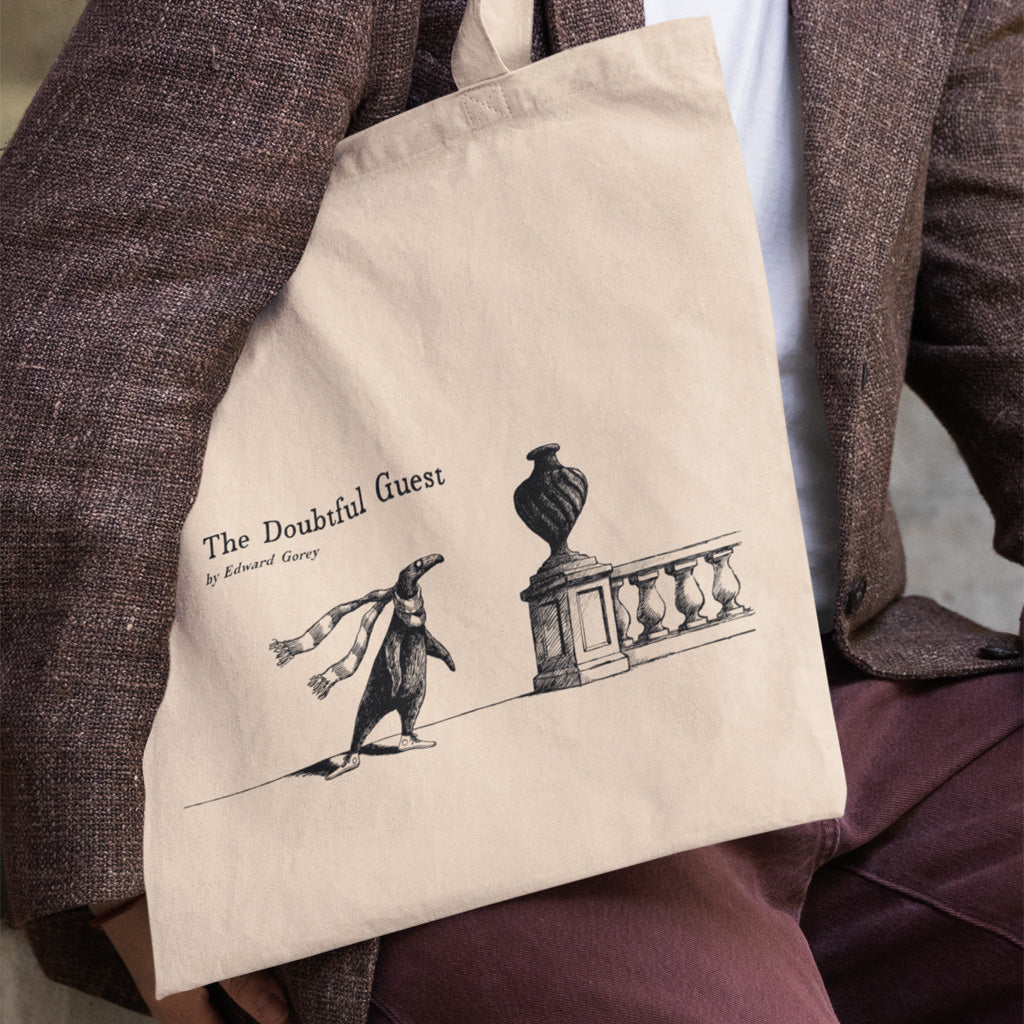 The Doubtful Guest tote bag featuring Edward Gorey illustration, held by person in brown jacket