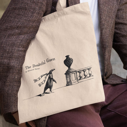 The Doubtful Guest tote bag featuring Edward Gorey illustration, held by person in brown jacket